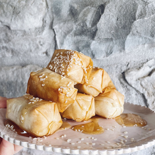 A stack of filo-wrapped Greek Style cheese, topped with sesame seeds and drizzled with a vegan honey alternative.